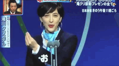 a woman in a suit and scarf stands in front of a microphone with chinese writing on the bottom