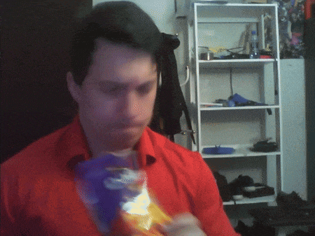 a man in a red shirt eating a bag of chips