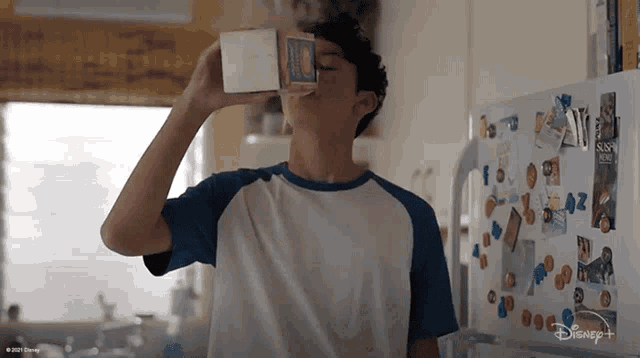 a boy is drinking milk from a carton in front of a disney + fridge
