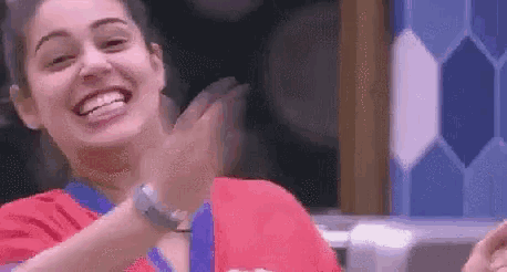 a woman in a red shirt is smiling and clapping her hands in a kitchen .