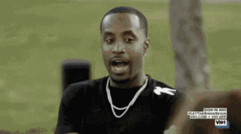 a man wearing a necklace and a black shirt is talking to someone .
