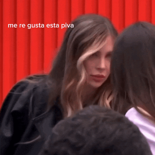 a woman in a black jacket stands in front of a red wall and says me re gusta esta pipa