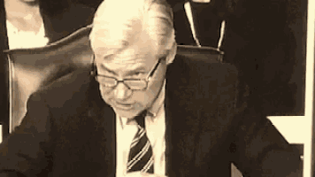 a man in a suit and tie is sitting in a chair looking down .