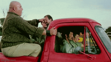 a group of men are sitting in the back of a red truck and one of them is holding another man 's hand