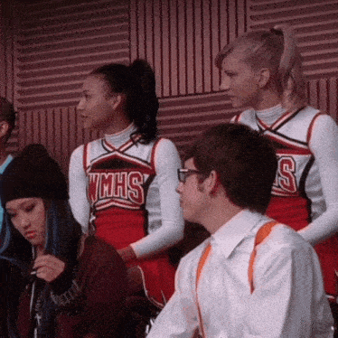 two cheerleaders wearing wmhs uniforms sit next to a man in a white shirt