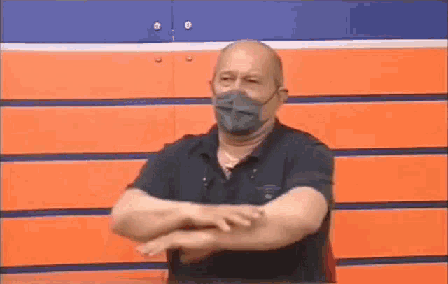 a man wearing a face mask is standing in front of a wall with his arms crossed .