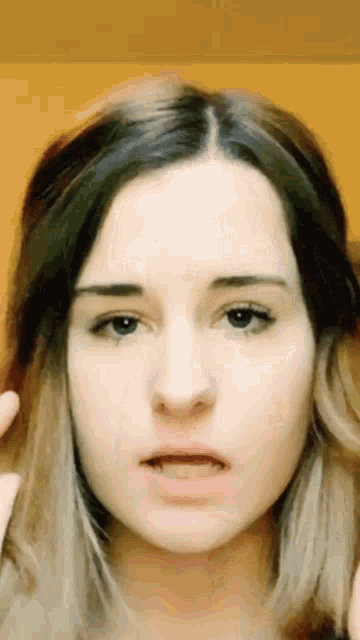 a close up of a woman 's face with a yellow wall in the background