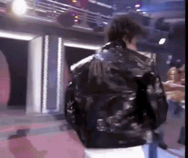 a man in a black leather jacket with the number 41 on the back is standing in a room .