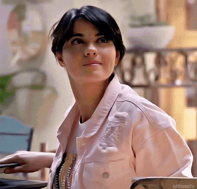 a woman wearing a pink jacket is sitting at a table with a book