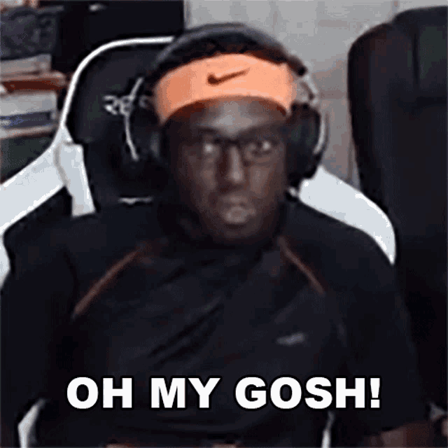 a man wearing headphones and an orange nike headband is sitting in a chair and saying oh my gosh .