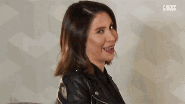 a woman is wearing a black leather jacket and making a funny face .
