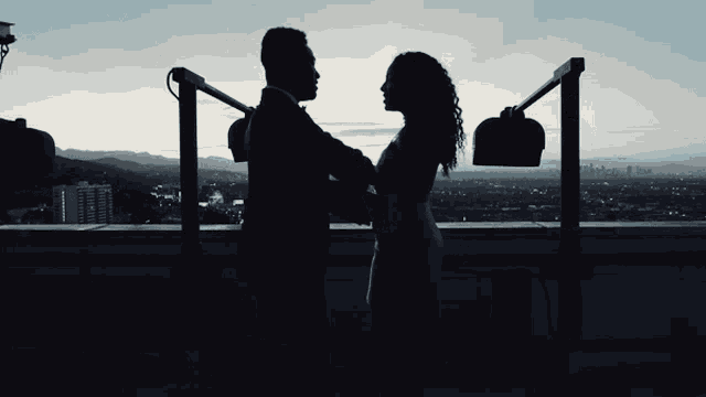 a silhouette of a man and woman standing on a rooftop with a city in the background