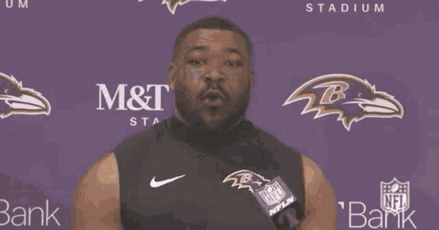 a man wearing a black ravens jersey stands in front of a purple wall