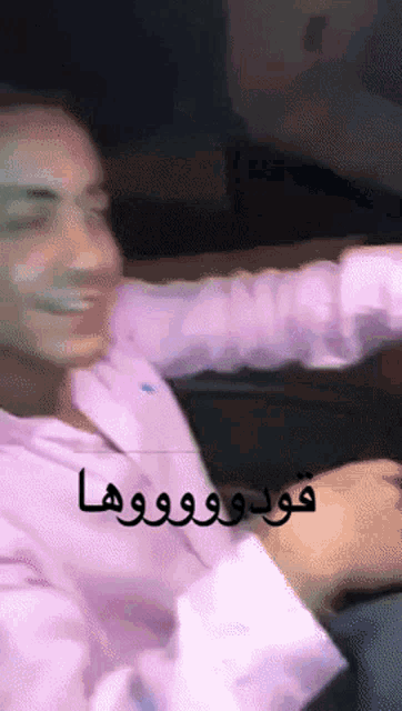 a man in a pink shirt is sitting on a couch with arabic writing on the bottom