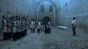 a man in a white shirt stands in front of a group of soldiers firing guns
