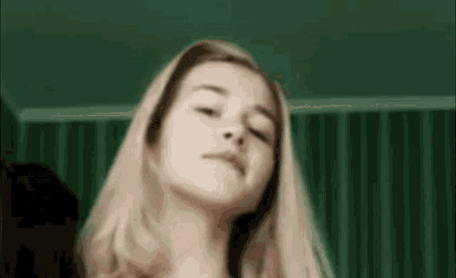 a close up of a woman 's face with her eyes closed in a room with green curtains .