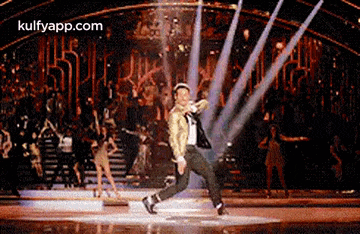 a man is dancing on a stage in front of a crowd while wearing a hat .