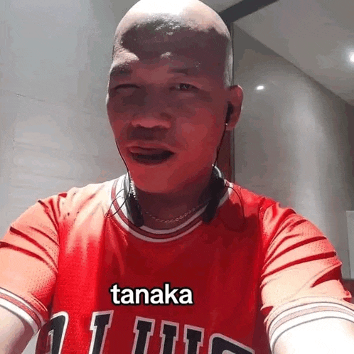 a bald man wearing a red shirt with the word tanaka on it .
