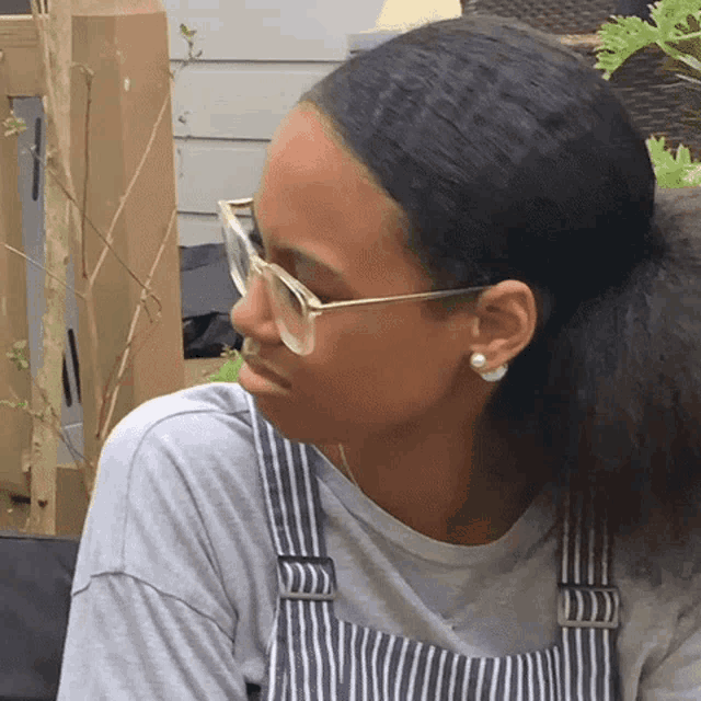 a woman wearing glasses and overalls is looking to the side