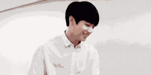 a young man wearing a white shirt and earrings is smiling and looking at the camera .