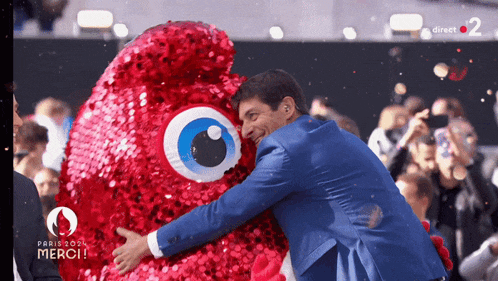 a man in a blue suit is hugging a stuffed animal that says paris 2024 merci