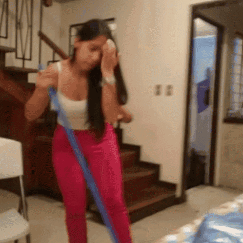 a woman wearing pink pants and a white tank top holds a blue mop
