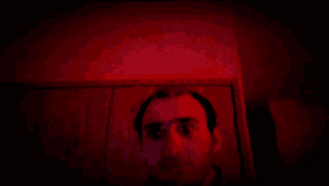 a man 's face is shown in a dark room with a red light behind him