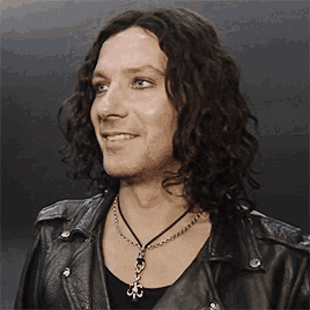 a man with long curly hair is wearing a black leather jacket and necklace