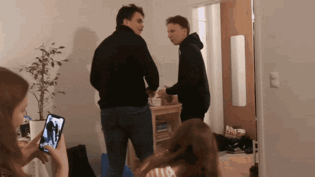 a man in a black hoodie is standing in a room with two other people