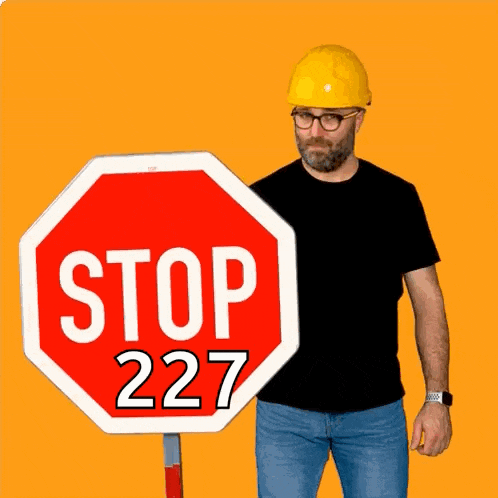 a man wearing a hard hat stands next to a large stop sign