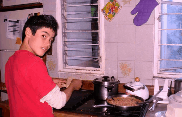 a boy in a red shirt is cooking on a stove
