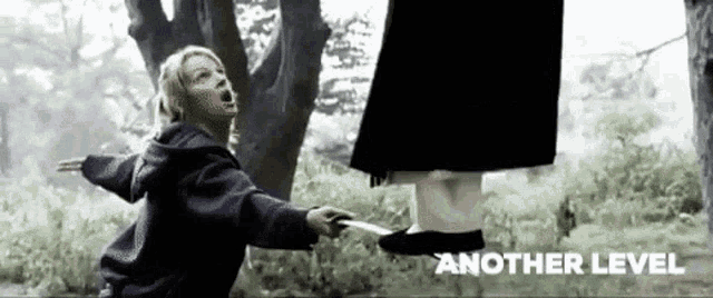 a young girl is holding a knife in front of a ghost hanging from a tree .