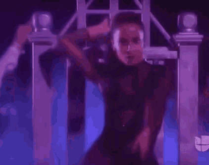 a woman is singing into a microphone while standing in front of a purple fence .