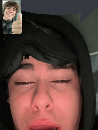 a man in a black hoodie is giving a thumbs up to another man on a video call