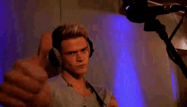 a man wearing headphones is standing in front of a microphone in a room .