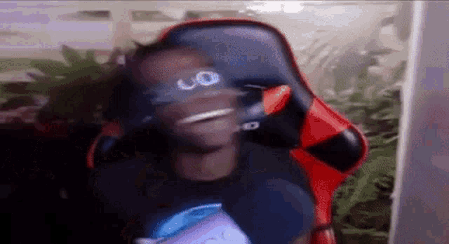 a man is sitting in a red and black gaming chair wearing sunglasses and headphones .