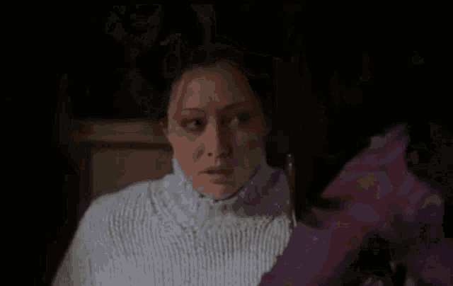 a woman in a white sweater is looking at another woman in a purple shirt in a dark room .