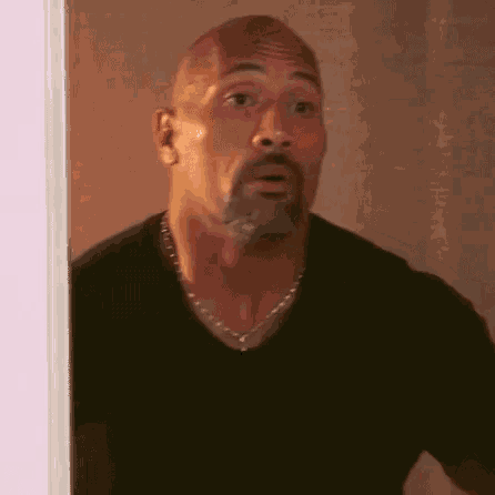 a bald man with a beard wearing a black shirt and a necklace is standing in a doorway .