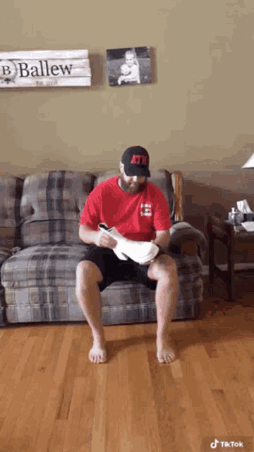 a man is sitting on a couch wearing a hat that says ath on it .