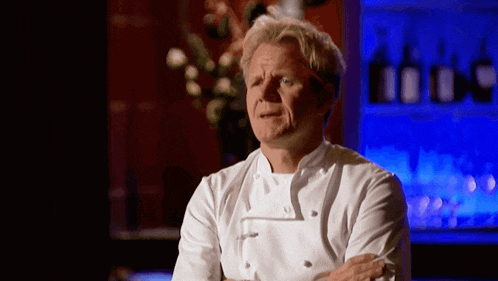 a man in a white chef 's jacket is standing with his arms crossed