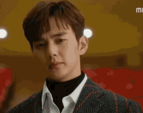 a young man in a suit and turtleneck is standing in front of a red seat .