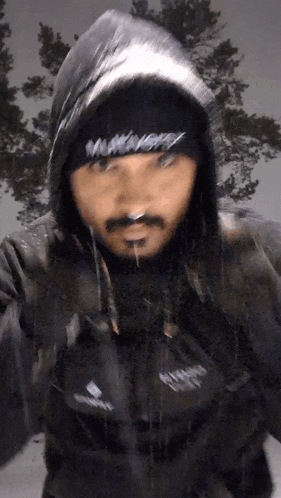 a man wearing a hooded jacket and a beanie with the word hungry on it is standing in the rain