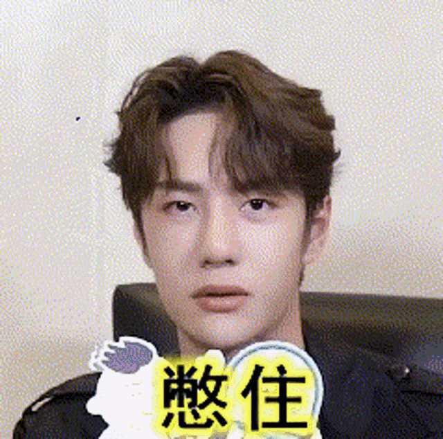 a young man is sitting on a couch and making a funny face with chinese characters .