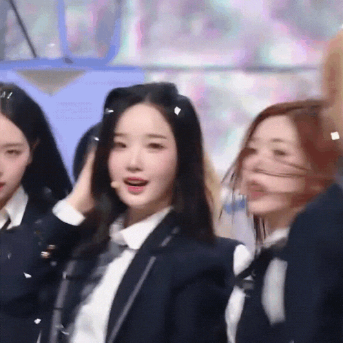 a girl in a suit and tie adjusts her hair while standing next to two other girls