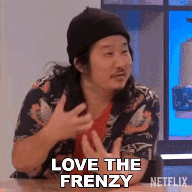 a man is sitting at a table with his hands out and says love the frenzy