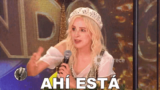 a woman is holding a microphone and says " ahi esta " in spanish