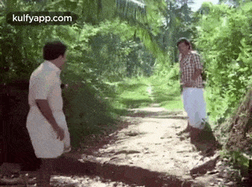 two men are standing on a dirt path in the woods .