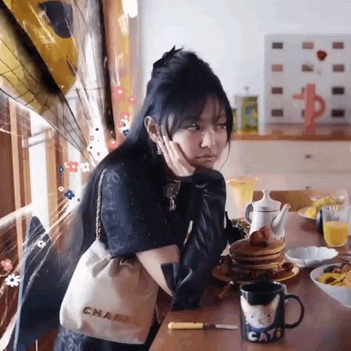 a woman sits at a table with a stack of pancakes and a cat mug