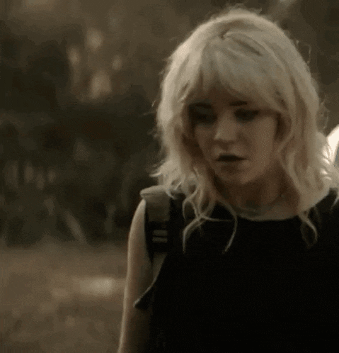 a woman with blonde hair and a black shirt is standing in the dark .