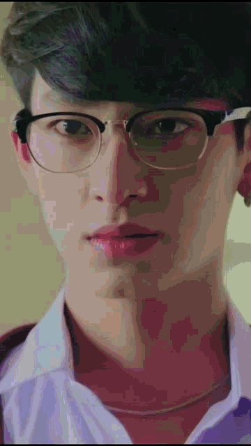 a young man wearing glasses and a white shirt looks at the camera